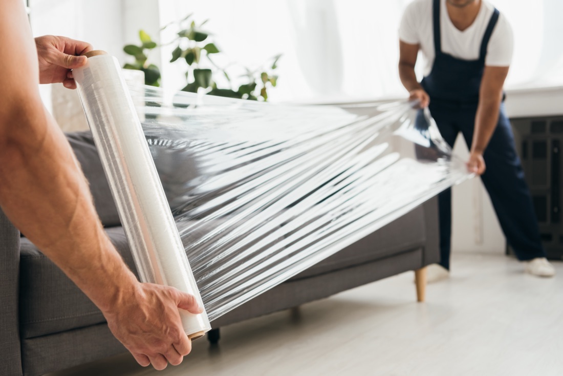 Two movers wrapping a sofa in protective stretch film