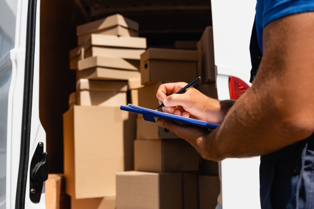 A mover loading cardboard boxes into a moving truck with a checklist