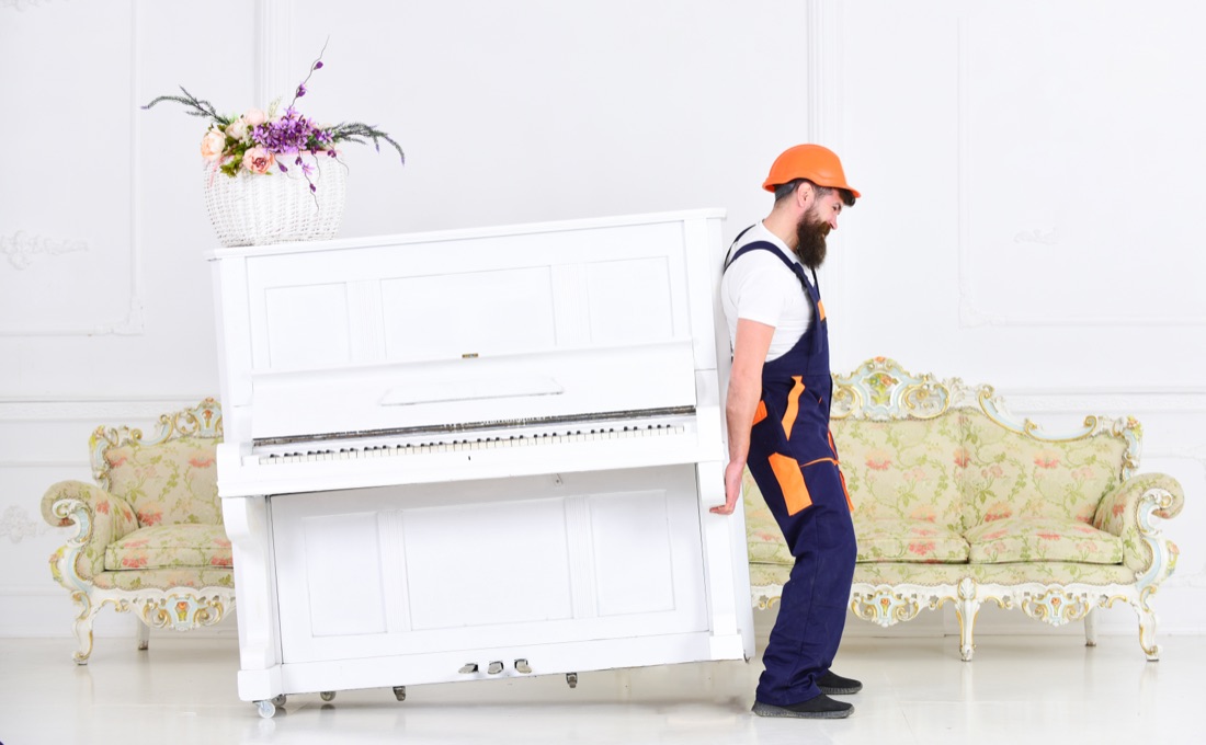 A mover carefully carrying an upright piano